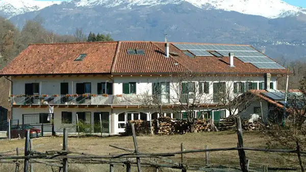 Edificio con pannelli solari, forse parte della comunità Damanhur, con montagne innevate sullo sfondo.