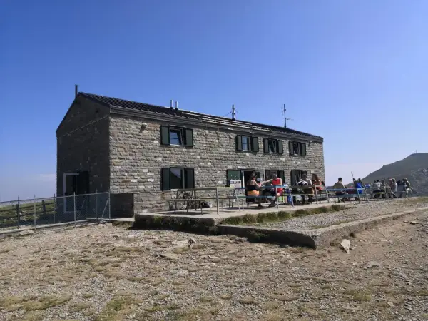 Rifugio in pietra con persone sedute ai tavoli all'esterno, un luogo ideale per una pausa durante un'escursione nei rifugi Emilia Romagna.