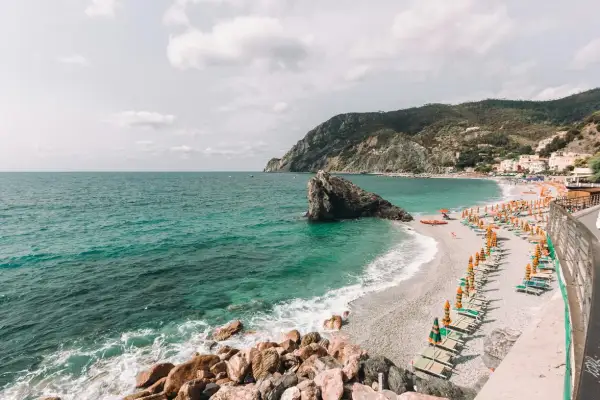 Spiagge libere Liguria: mare turchese, scogli imponenti e file di ombrelloni colorati su una spiaggia di ciottoli.