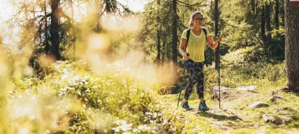 Giovane donna con bastoncini da trekking si gode le sue passeggiate Trentino in un bosco soleggiato.