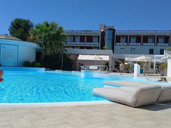 Piscina azzurra e lettini prendisole in un resort, con un edificio moderno sullo sfondo. Un'oasi di benessere e relax, perfetta per godersi le terme Viterbo Salus.