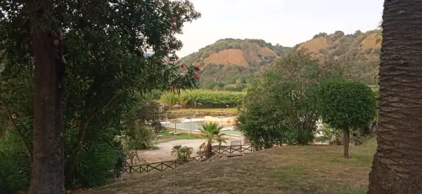 Un angolo di pace ad Agnano, dove si trova un complesso con piscine e vegetazione lussureggiante, incorniciato da colline verdi.