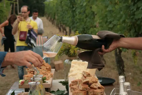 Un brindisi nel Val Tidone: bollicine versate in un calice, circondate da focaccia e formaggio, con vigneti sullo sfondo.