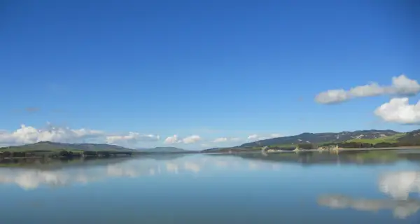 Lago calmo con riflessi di colline verdi e cielo azzurro. Un'ottima meta per scoprire cosa vedere vicino Matera.