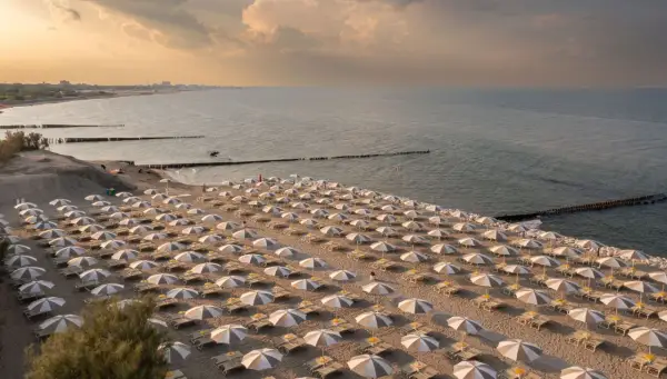 Filetto di sabbia dorata con file ordinate di ombrelloni e lettini, bagnato dal mare del Friuli Venezia Giulia al tramonto.