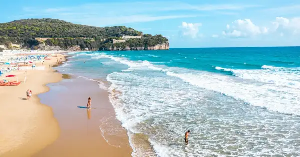 Spiaggia dorata con onde azzurre, scogliere verdi e un castello in cima. Perfetto per chi cerca il mare nel Lazio dove andare.