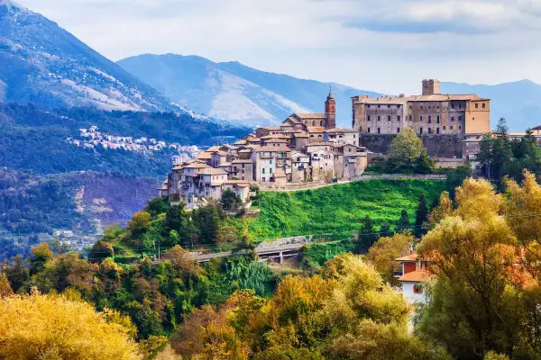 Borgo medievale su una collina verde, con montagne sullo sfondo. Un gioiello di montagna vicino Roma, con case antiche e un castello imponente.