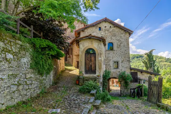 Un vicolo lastricato conduce a un antico portone in legno. La scola di pietra, con edera rampicante, sembra uscita da un libro di fiabe.