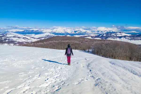 Escursionista in un paesaggio innevato, ideale per scoprire dove andare sulla neve vicino Roma. Montagne imbiancate all'orizzonte.