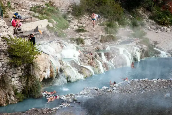 Persone si rilassano nelle acque fumanti delle terme di Petriolo, tra rocce calcaree e vegetazione.