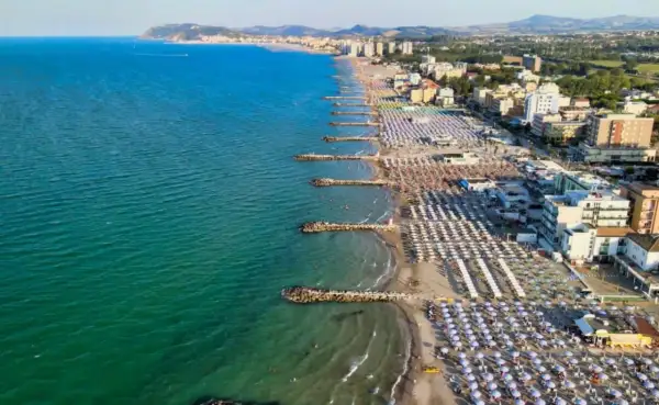 Vista aerea di una spiaggia affollata con ombrelloni colorati e il mare azzurro, tipica di una città riviera romagnola.