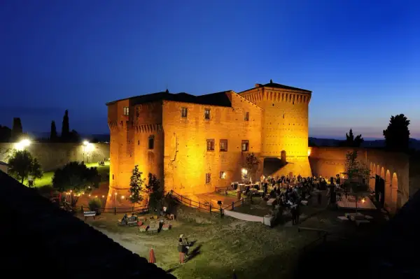 Rocca Malatestiana illuminata di sera, con persone che socializzano e godono dell'atmosfera. Un luogo suggestivo da scoprire tra le cose da vedere a Cesena.