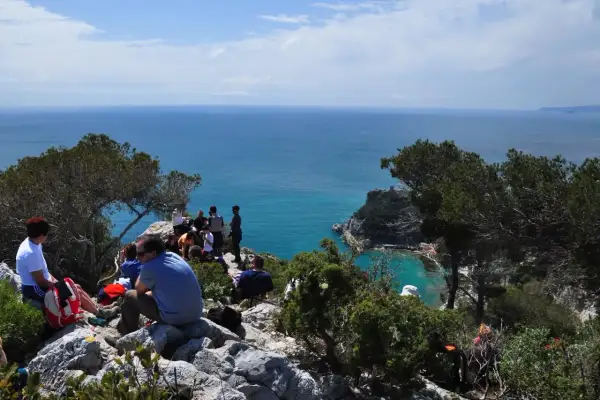 Gruppo di persone in pausa durante un trekking a Finale Ligure, con vista sul mare azzurro e scogliere.