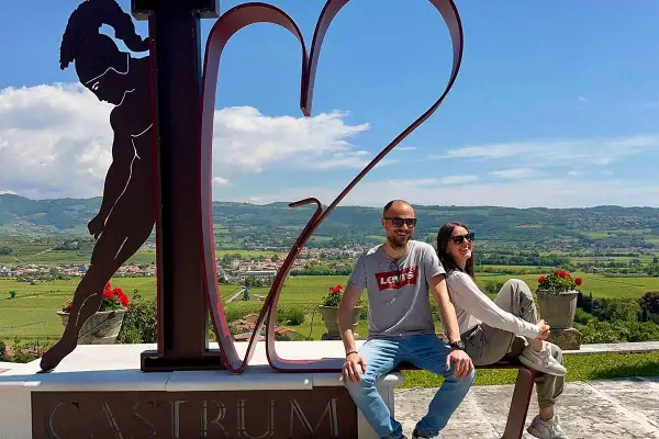 Co zobaczyć w Valpolicella: para siedzi na ławce przed rzeźbą serca i postacią, z widokiem na winnice i wzgórza.