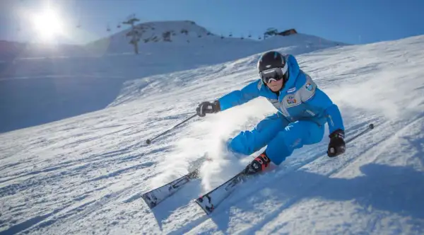 Sciatore in azione su una pista innevata, tipica delle località sciistiche Piemonte, con sole splendente e skilift sullo sfondo.