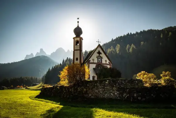 Chiesa di San Giovanni in Ranui, incastonata nel **Val di Funes**, con le Dolomiti sullo sfondo illuminate dal sole.