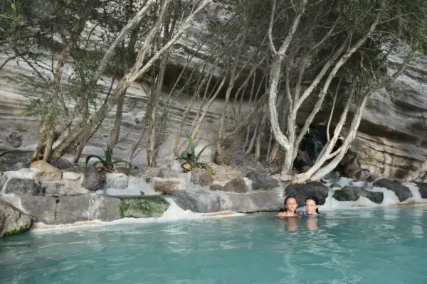 Due bambine si godono le terme libere di Ischia, immerse in acque turchesi tra rocce e vegetazione rigogliosa.