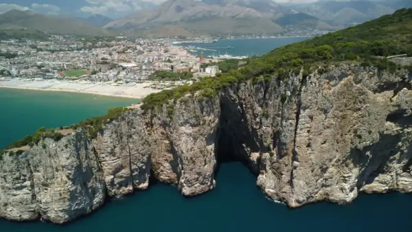 La leggenda della Montagna Spaccata a Gaeta: imponenti scogliere rocciose si tuffano nel mare blu, con la città sullo sfondo.