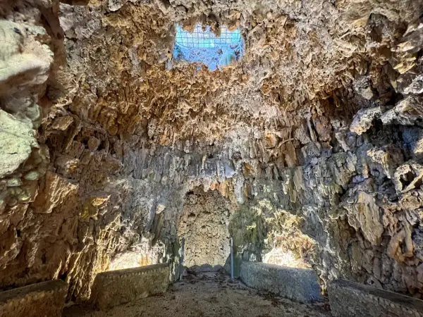 Interno di una grotta con stalattiti e stalagmiti, illuminata da una luce soffusa che filtra da un'apertura in alto. Sembra il ventre del **colosso dell'Appennino**.