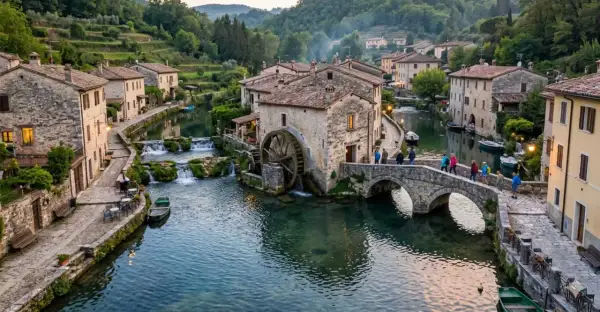 Un incantevole borgo italiano, una vera citta sull'acqua, con case in pietra, un mulino ad acqua e un ponte pittoresco attraversato da persone.