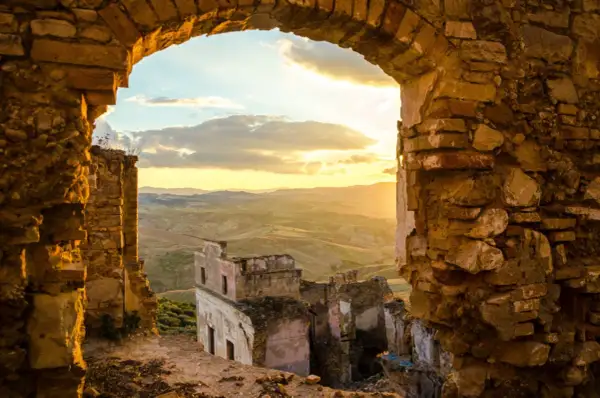 Rovine di **paesi abbandonati in Italia** illuminate dal tramonto, con colline ondulate all'orizzonte.
