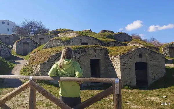 Pietragalla cosa vedere: antiche case-grotta scavate nella collina, con una donna che le osserva. Un luogo suggestivo da esplorare.