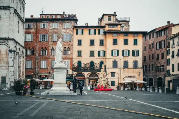 La piazza di Lucca con la statua bianca, edifici storici e un albero di Natale decorato.