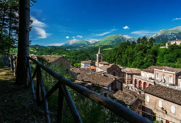 Borgo pittoresco nei Monti Sibillini, cosa vedere: tetti in cotto, campanile e montagne verdi.