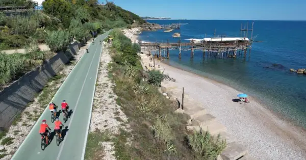 Ciclisti lungo la via verde della costa dei trabocchi, con il mare blu e le antiche macchine da pesca sullo sfondo.
