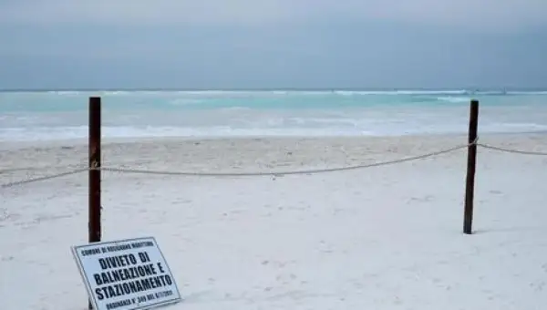 Spiagge bianche deserte con mare turchese. Un cartello vieta balneazione e stazionamento.