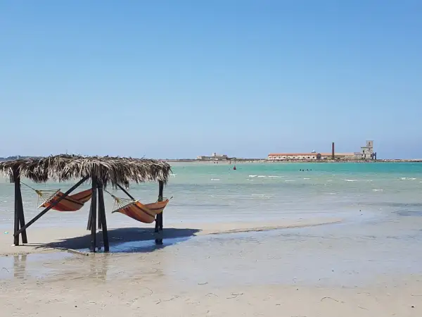 Amache colorate sotto un tetto di paglia, con il mare turchese e antichi edifici all'orizzonte. Un angolo di paradiso a San Teodoro, spiaggia rosa.