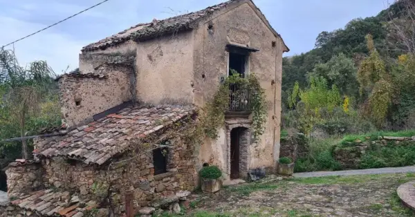 Antica casa in pietra, parte di una città fantasma umbria, con tetto in tegole rotte e vegetazione che cresce ovunque.