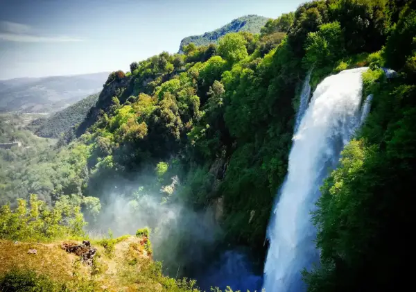Cascata imponente nella rigogliosa montagna umbria, con valli verdi e cielo azzurro.