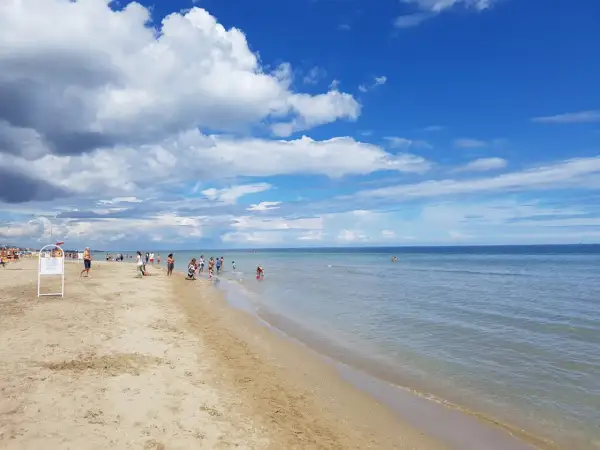 Giornata di sole e nuvole sul mare di Riccione. Bambini giocano sulla battigia mentre adulti passeggiano sulla sabbia dorata.
