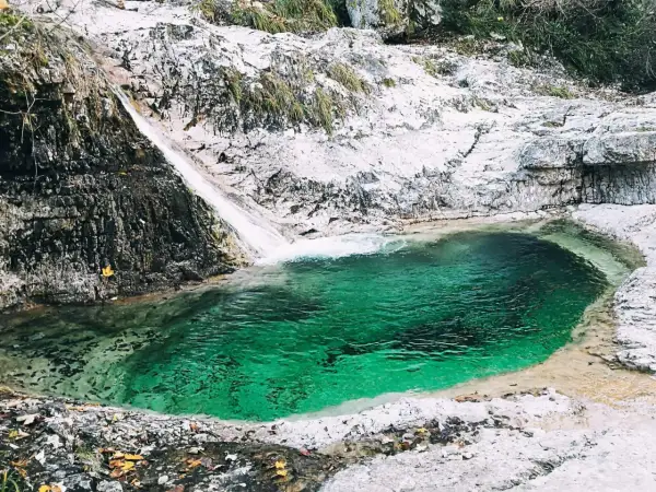 Cascata e pozza smeraldo nella valle del Mis, con rocce bianche e vegetazione.