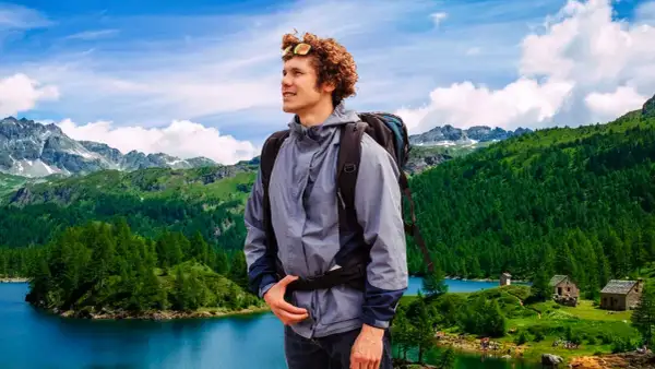 Giovane escursionista con zaino ammira un paesaggio alpino con laghi e boschi nel Piemonte.