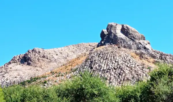 Rocciosa cresta nella Planargia, Sardegna, sotto un cielo azzurro. Vegetazione verde rigogliosa in primo piano.