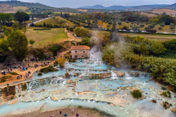 Cascate naturali con acqua azzurra e gente che si rilassa, un vero spettacolo di arte terme in un paesaggio collinare.