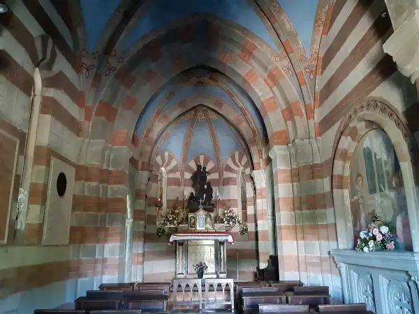 Interno di una cappella con volte a crociera a strisce rosse e bianche. Al centro, un altare con statue e fiori. Un esempio di cosa vedere a Berceto.