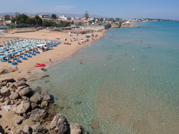 Una spiaggia affollata con lettini e ombrelloni, bagnanti in acqua e due kayak rossi sulla sabbia. Il noto mare cristallino invita a un tuffo.
